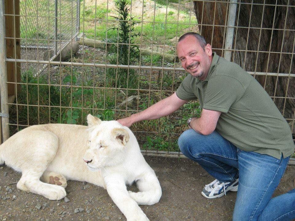 Geoff Hughes kneeling down smiling outside patting a white leopard